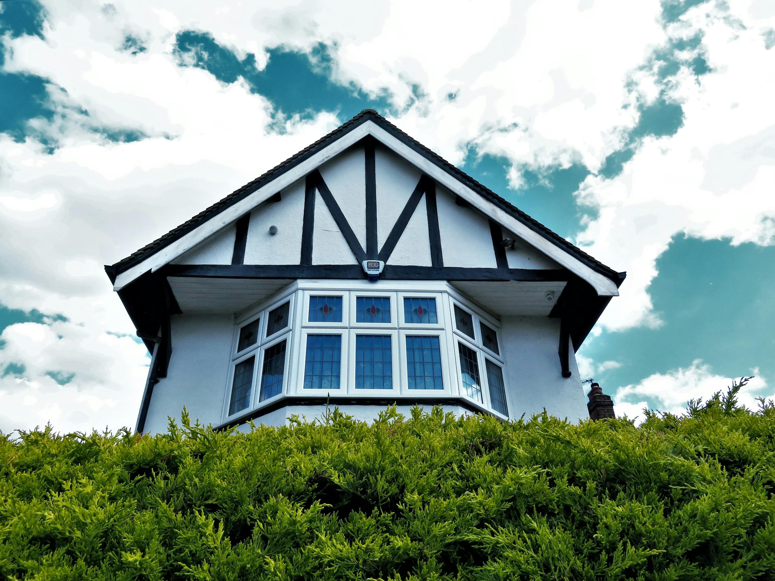 Tudor-style house facade with a bay window against a vibrant sky and greenery.
